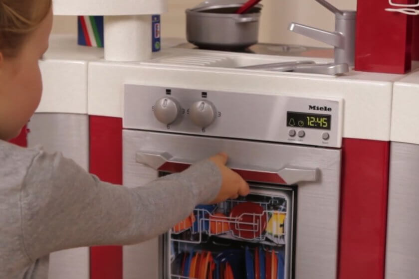 Mädchen räumt Spülmaschine ihrer Spielküche ein