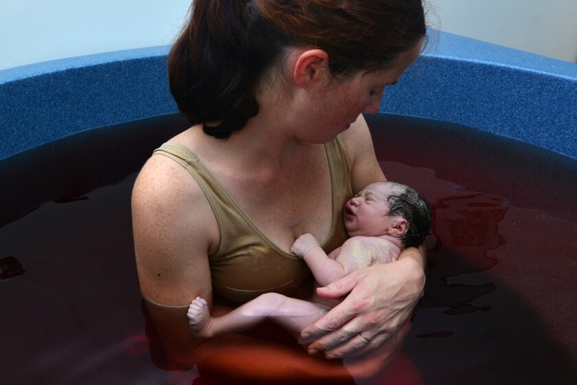Frau hält Baby nach Wassergeburt