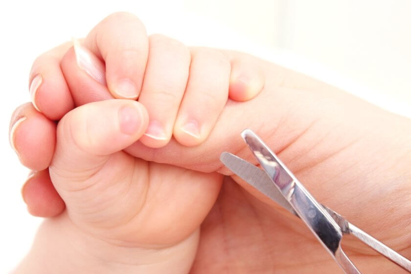 Mutter schneidet Baby die Fingernägel mit Nagelschere aus Babypflegeset
