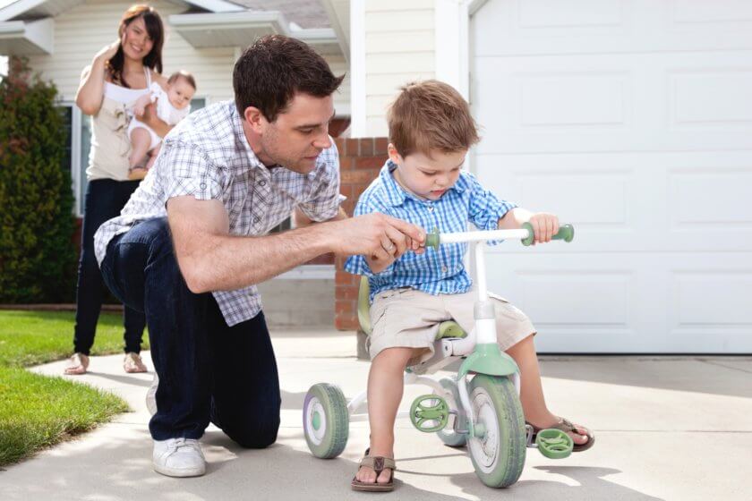 Kind lernt das Dreiradfahren und bekommt von Papa Hilfestellung