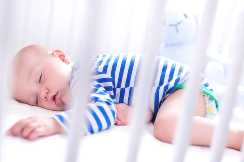 Baby schläft gemütlich im weißen Gitterbett