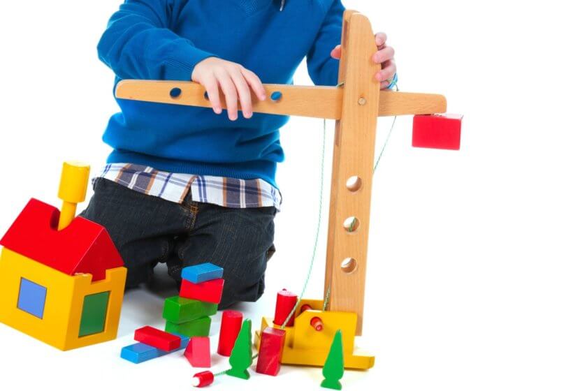Junge spielt mit Holzkran und Bausteinen im Kinderzimmer